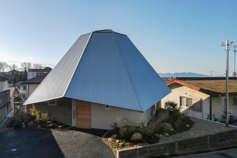 Exterior view of the pyramidal metal roof over plywood walls with a landscaped gravel yard