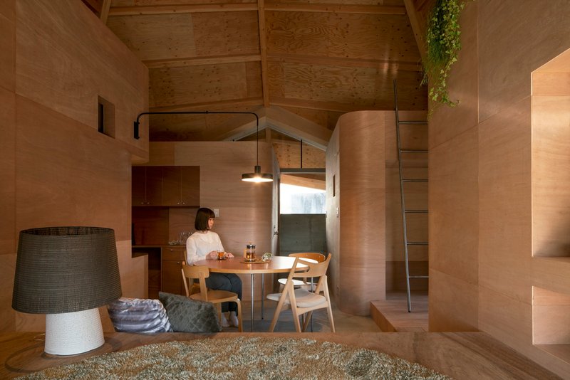 Dining area with timber table and chairs framed by plywood walls and pendant light fixture