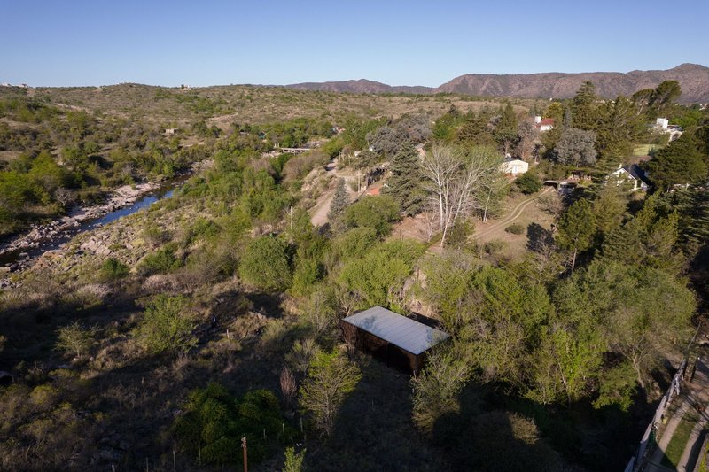 Aerial view of the elevated timber cabin nestled among native trees along a winding river valley