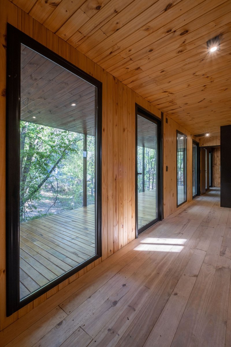 Interior corridor with timber walls and ceiling and black-framed glazing overlooking a deck