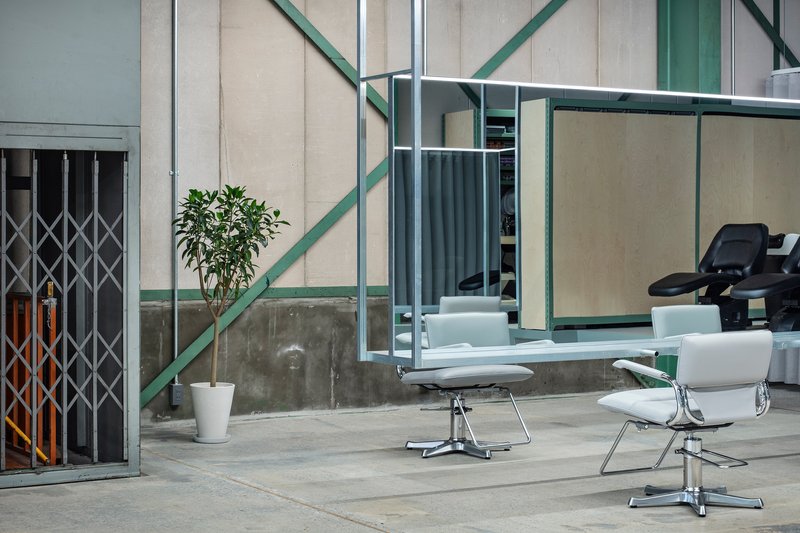 Two styling chairs on polished concrete floor beside a folding metal gate and potted plant