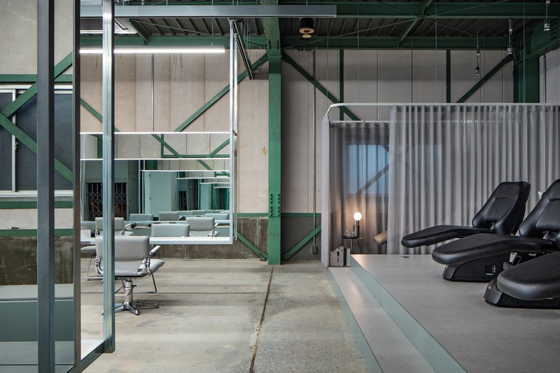 View through green steel frame toward reclined washing chairs behind a curved curtain screen