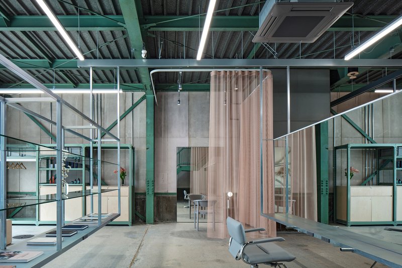 Interior salon workspace with exposed green steel trusses and draped fabric partitions dividing stations