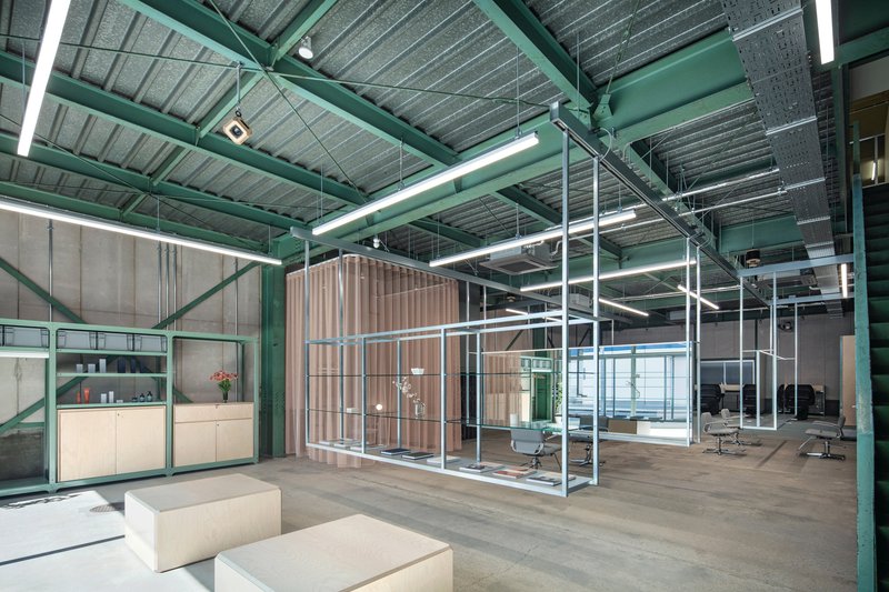 Open office interior with exposed green steel structure, corrugated slatted partitions and polished concrete flooring