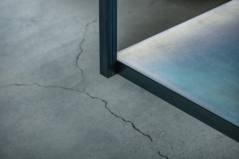 Detail of dark steel frame meeting polished floor surface with visible crack in concrete