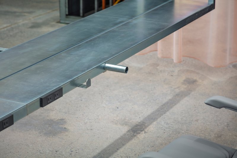 Integrated power outlet and cylindrical footrest mounted under steel desk edge on concrete floor