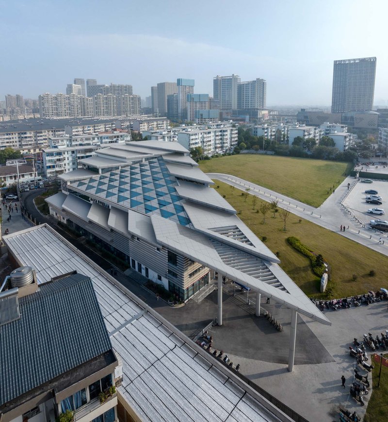 Angled aerial showing the layered roof planes and triangular canopy sheltering the entry plaza with pedestrians