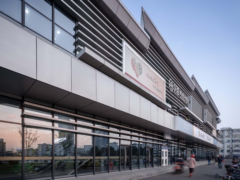 Layered facade with horizontal louvers and glazed storefront at dusk with pedestrians passing