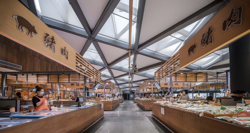 Interior market hall with timber-clad vendor stalls under an exposed steel truss and glazed roof structure