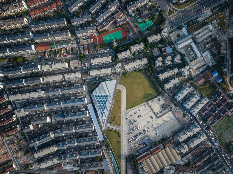 Drone view showing the angular roof geometry and adjacent parking lot within the dense urban fabric