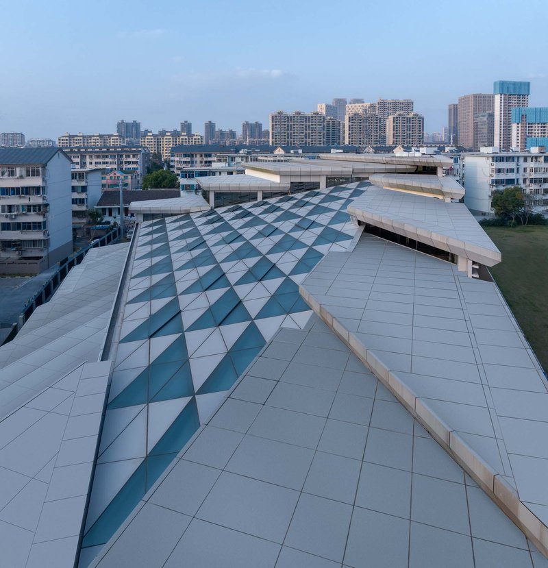 Rooftop view of the folded metal panel system with diagonal teal-tinted glazing at dusk