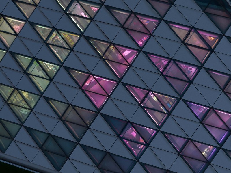 Close-up of the triangular glazed panels with pink and amber interior lighting at twilight
