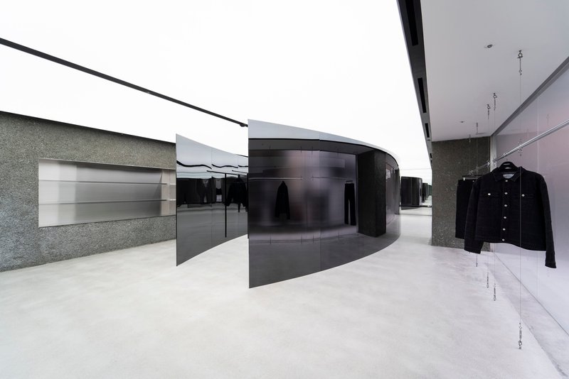 Retail interior with black curved partition walls and textured stone surfaces under a continuous skylight