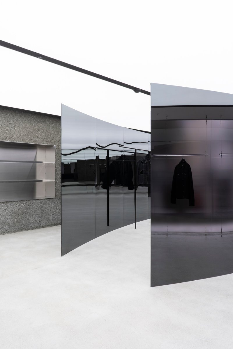 Retail interior with black glass partitions, terrazzo walls, and clothing racks under white painted ceiling