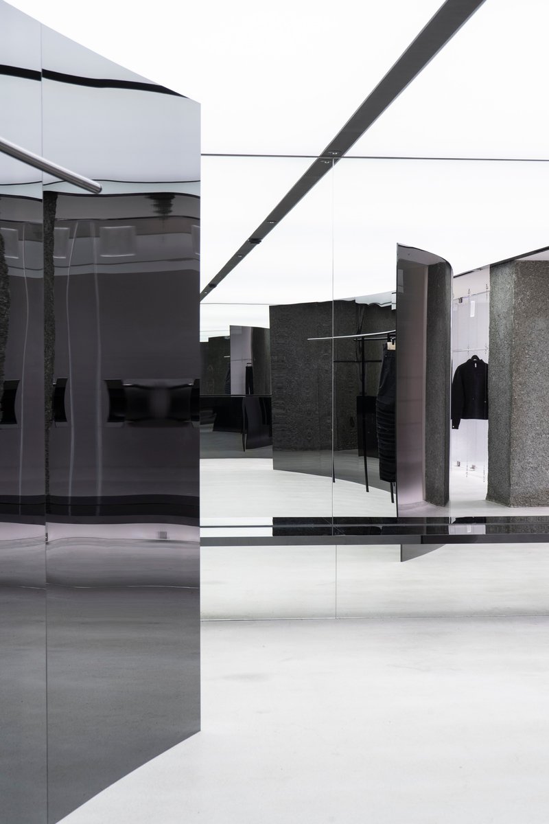 Open sales floor showing layered glass panels, curved dark metal displays, and polished terrazzo columns