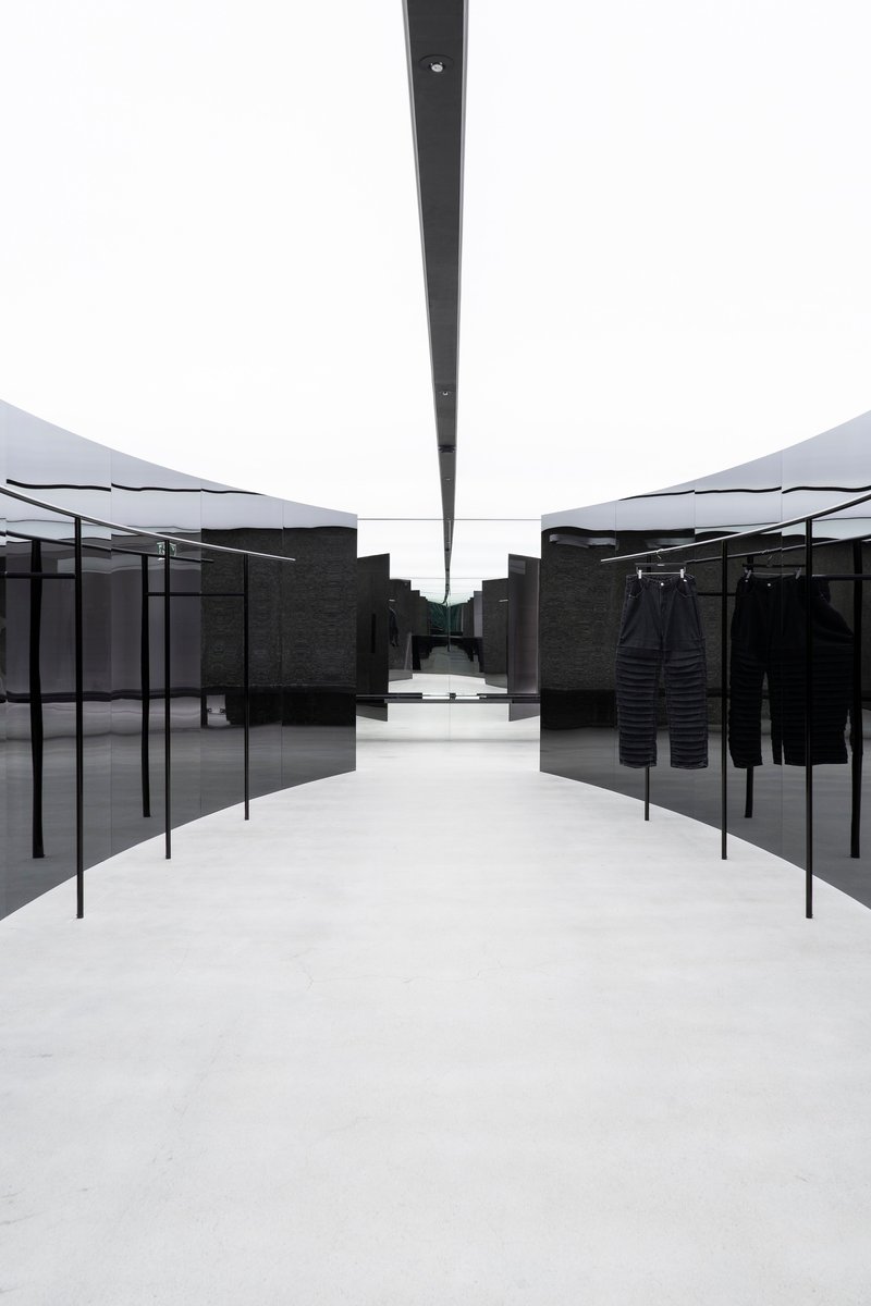 Central aisle framed by black metal garment racks beneath linear skylight slot in white ceiling