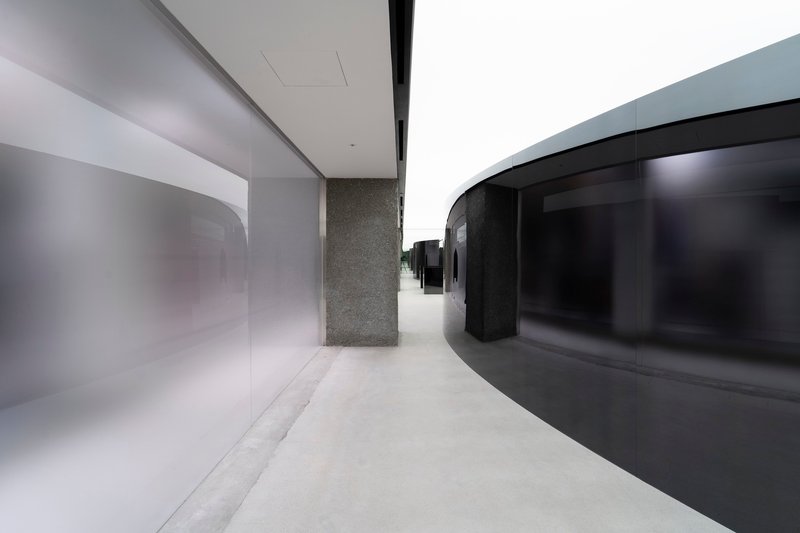 Curved circulation corridor with black glass facade, terrazzo column, and polished white resin floor