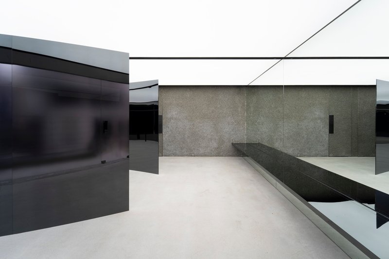 Angular black glass partitions intersecting with textured stone wall and built-in seating bench on polished floor