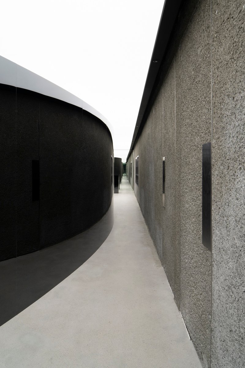 Narrow corridor between curved black wall and textured stone surface with vertical slot openings