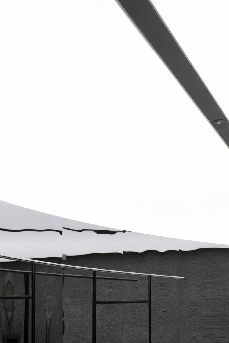 View of undulating white ceiling edge meeting textured dark stone wall with steel-framed glazing below