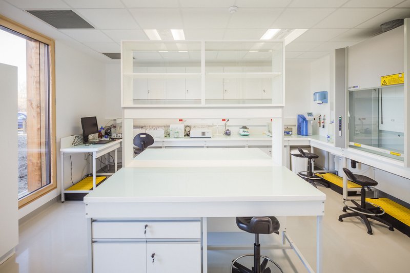 White laboratory interior with central benches, overhead storage cabinets and task stools