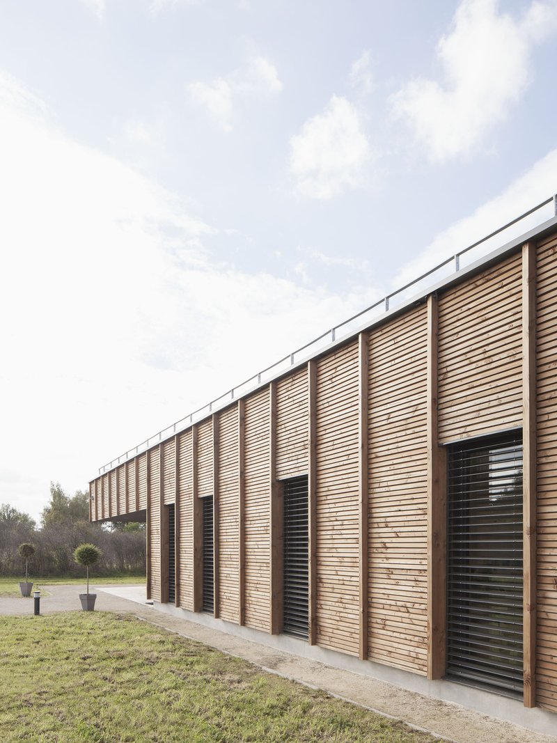 Curved facade of vertical timber slats with integrated black ventilation louvers under open sky