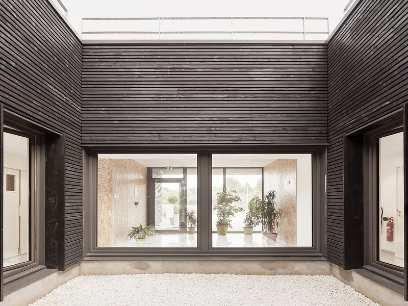 Interior courtyard with horizontally slatted charred timber walls and glazed doors opening to rooms with potted plants