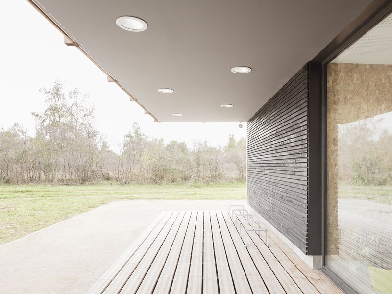 Covered timber deck with horizontal slatted flooring and charred wood cladding opening to a misty meadow landscape