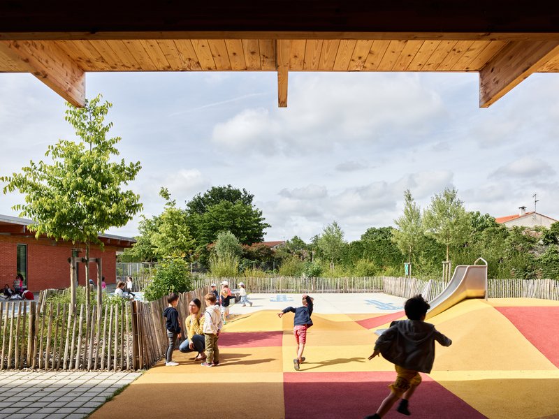 View from timber-clad porch toward playground with multicolored surfacing where children run and play