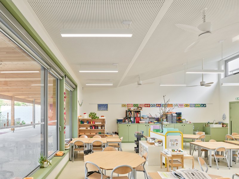 Interior classroom with perforated acoustic ceiling, hexagonal tables, and green storage cabinets along the wall