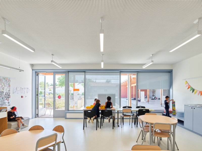 Classroom interior with perforated white ceiling panels and glazed doors opening onto a planted courtyard