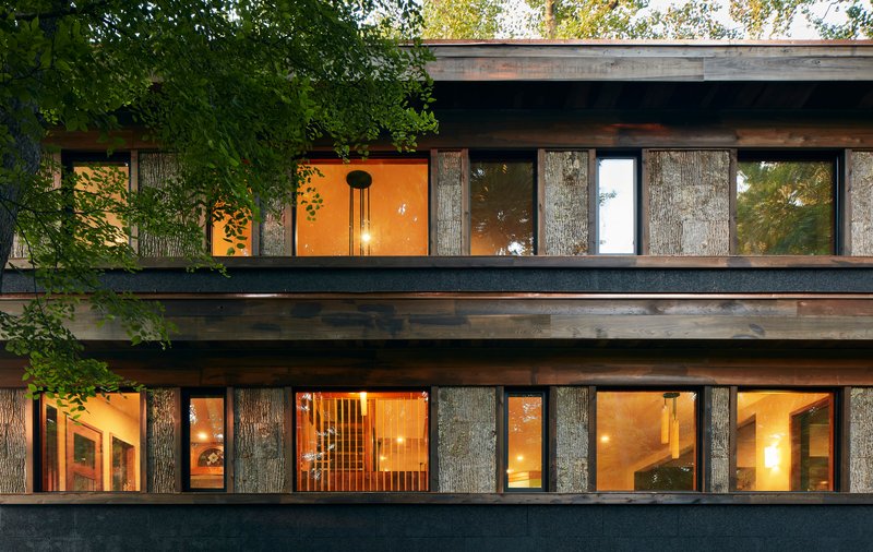 Two-storey facade with textured bark-clad columns between glazed bays at dusk
