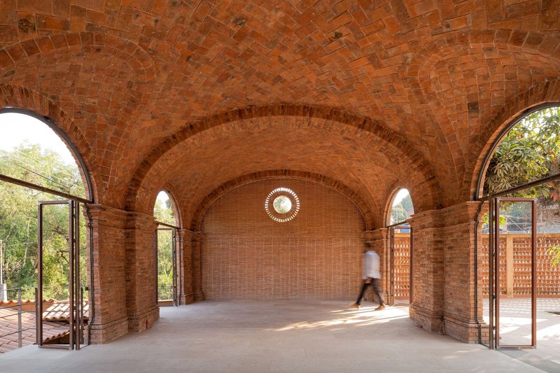 Interior of a brick vaulted hall with arched doorways and a figure walking through dappled sunlight