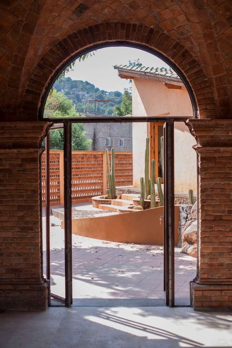 View through an arched brick doorway to a courtyard with planted beds and hills beyond