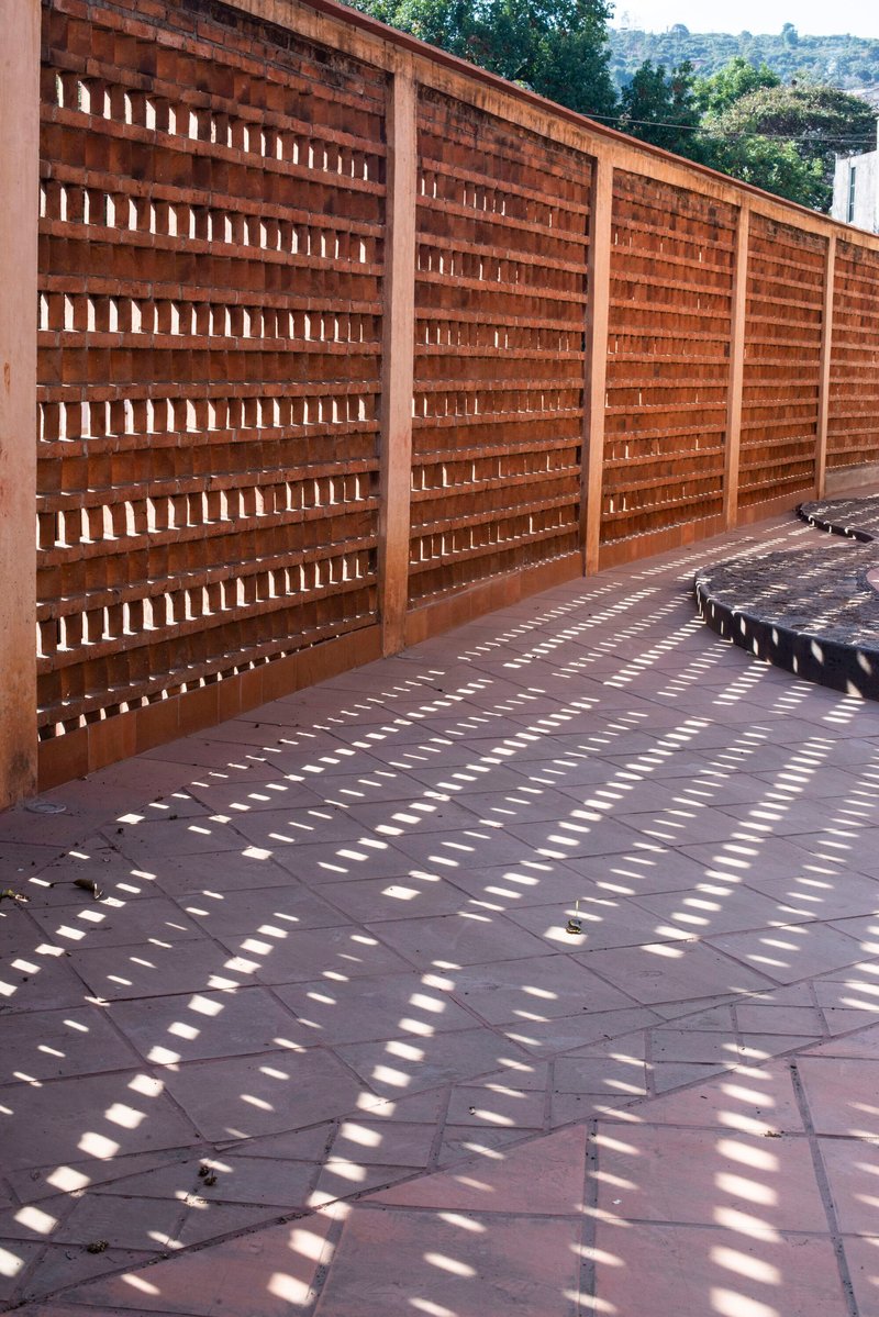 Perforated timber screen wall casting a pattern of shadows onto dark paving tiles below