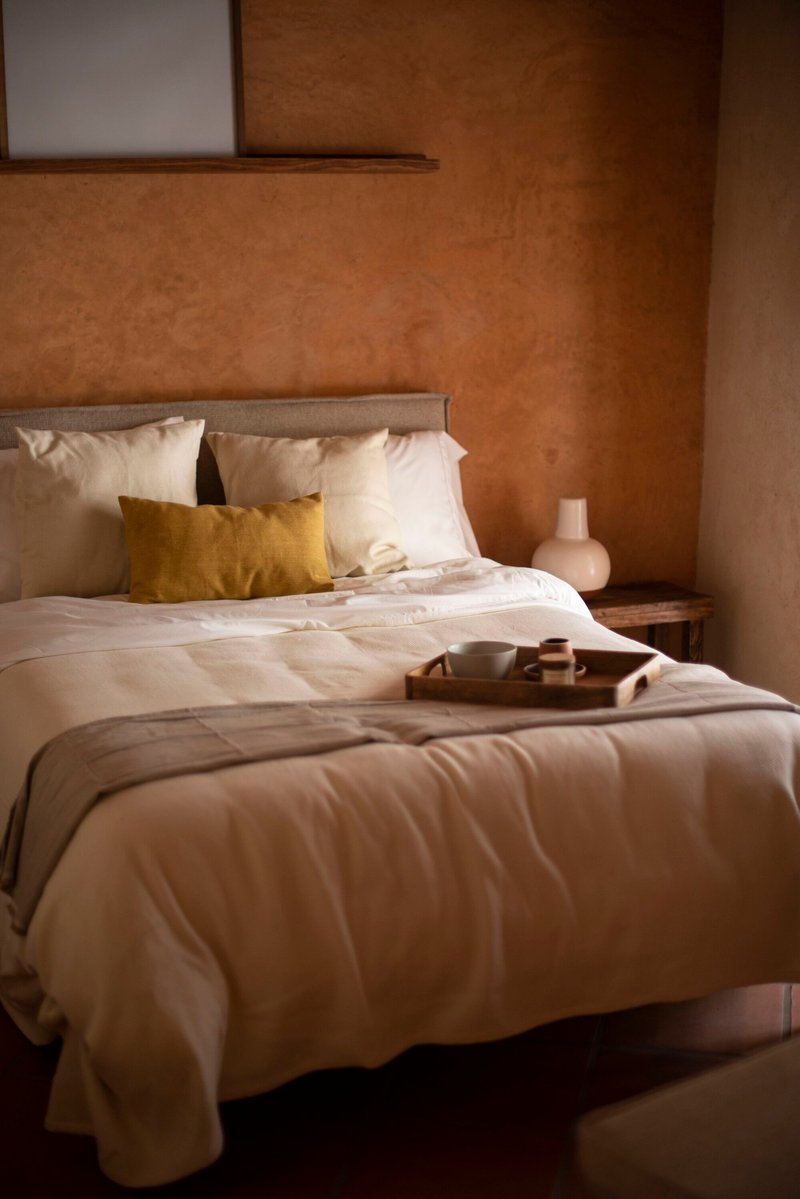 Bedroom with earthen plaster walls and white linens beneath a timber-framed clerestory window
