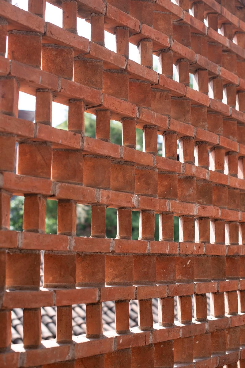 Perforated brick screen wall in running bond pattern filtering daylight and greenery beyond