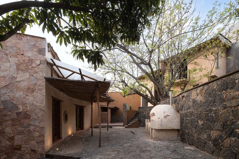 Courtyard view with stone walls, timber canopy, domed oven and bare tree under evening light