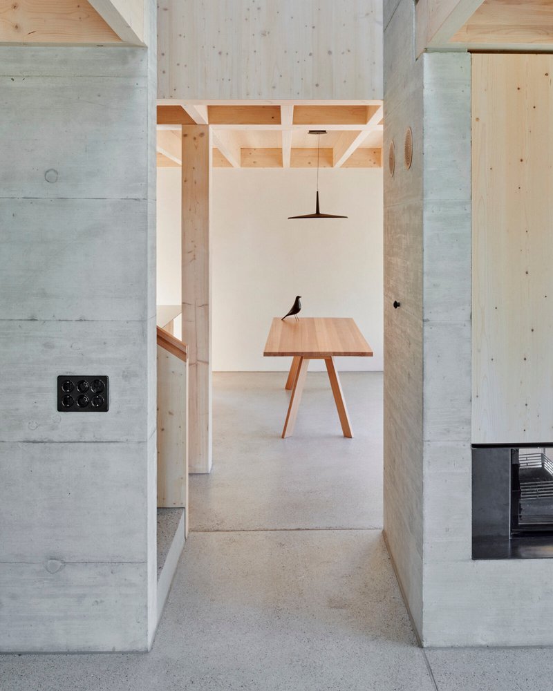 View through concrete walls into a dining area with exposed timber ceiling joists and pendant light