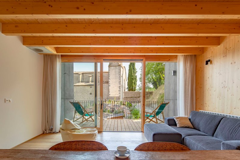 Living room with exposed timber beams and glazed doors opening to a balcony with two lounge chairs