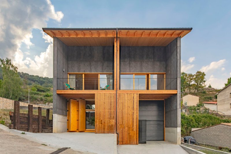 Street facade with vertical timber slats flanking a garage door beneath concrete panels and timber eaves