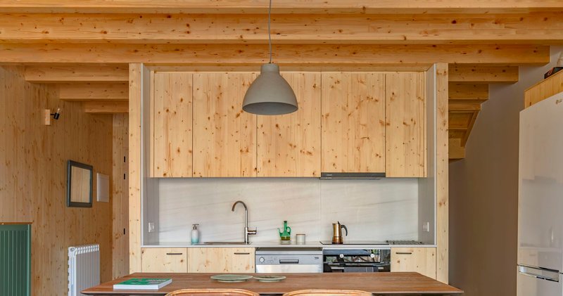 Kitchen with pale wood cabinetry, exposed timber ceiling beams and a grey pendant light