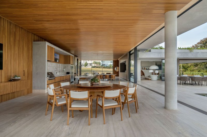 Open-plan living space with timber slatted ceiling and cylindrical concrete columns framing views to landscape