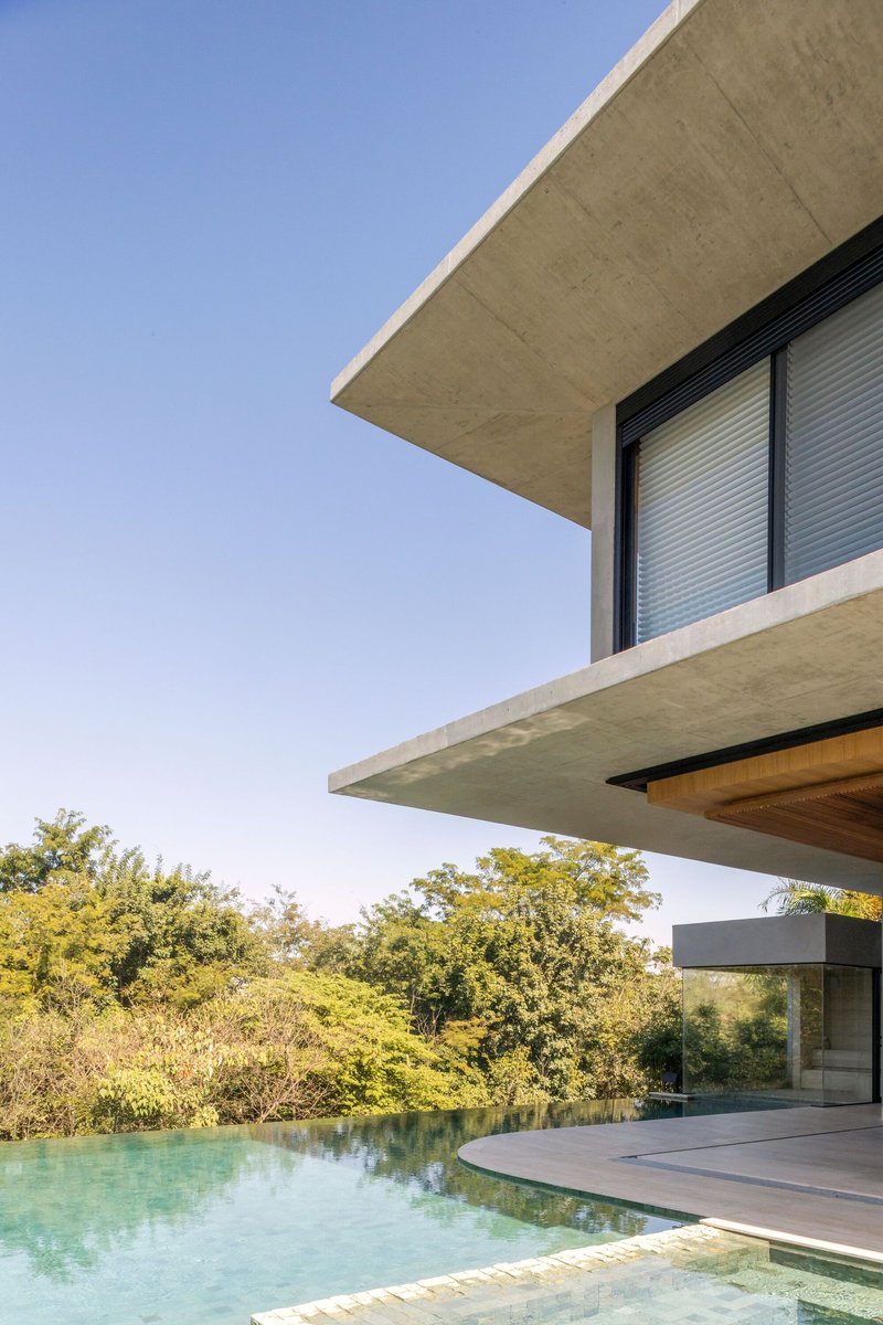 Cantilevered concrete terrace with shutter-clad window above infinity pool and surrounding trees
