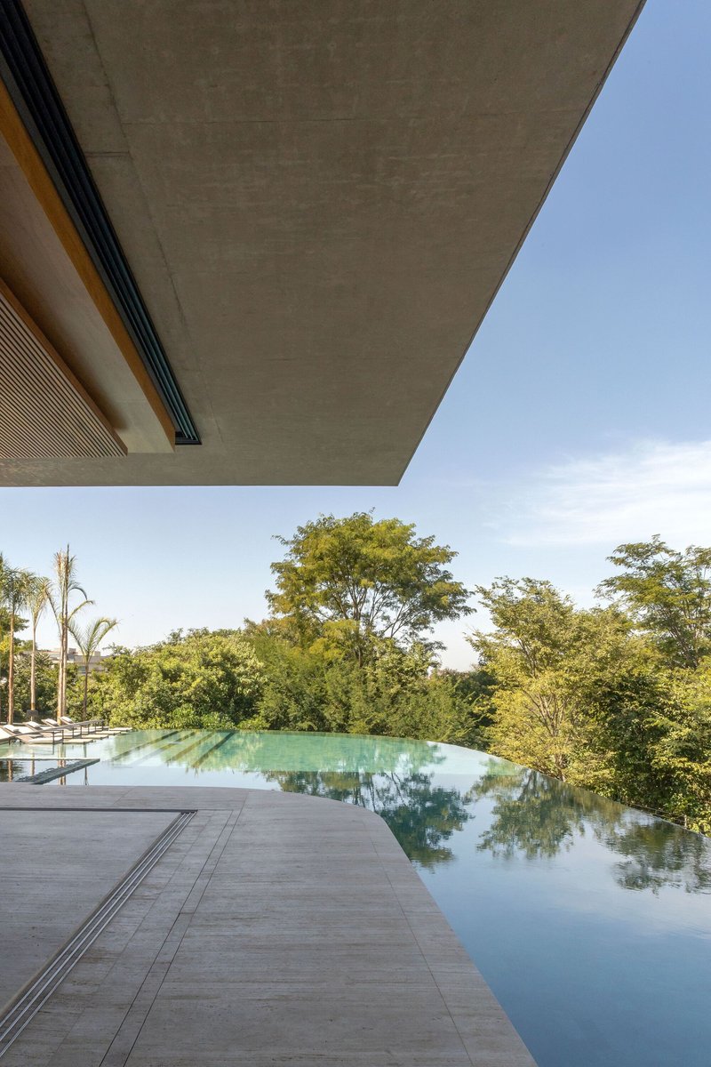 Infinity pool edge reflecting the surrounding trees beneath a concrete canopy soffit