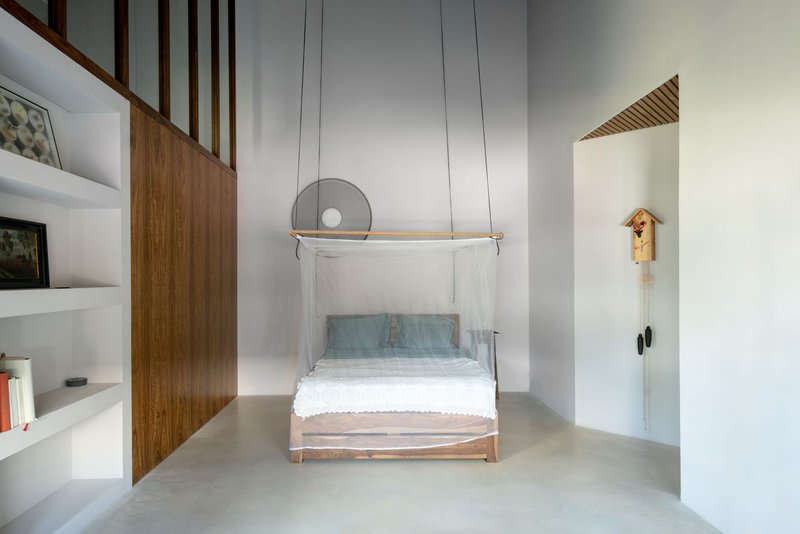 Bedroom with suspended timber bed frame and mosquito netting beneath vertical wood slats and high ceiling