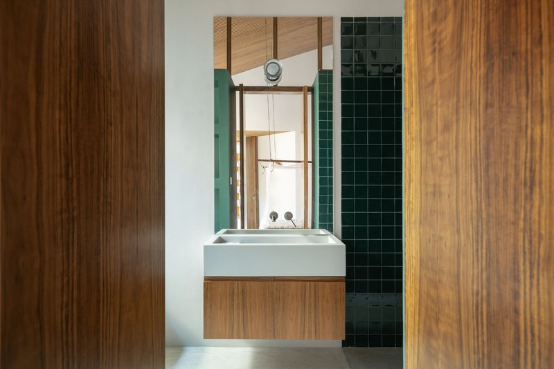 Bathroom vanity with timber cabinetry framed by wood panels and dark green tiled shower beyond