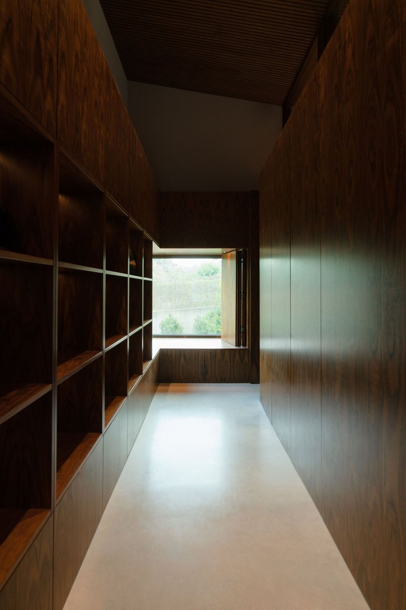 Timber-lined corridor with built-in shelving leading to window seat framed by afternoon light