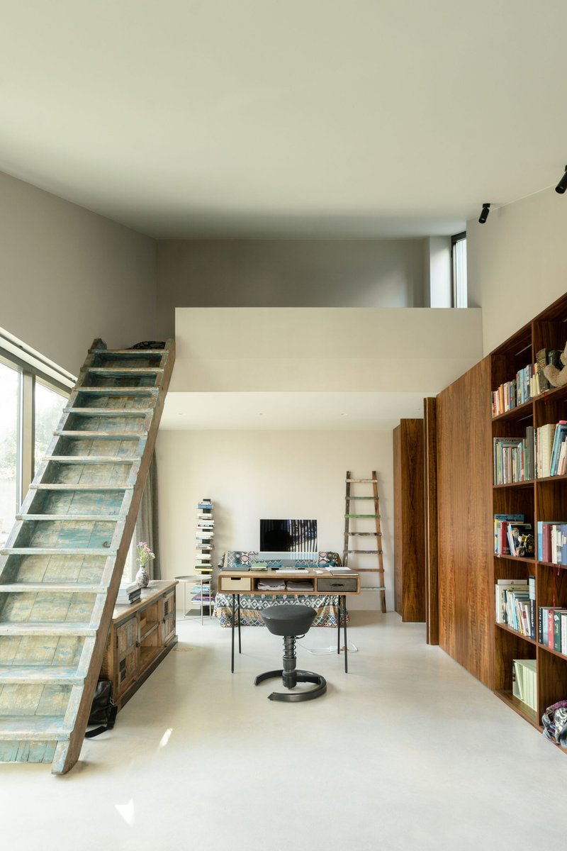Double-height interior with timber bookshelf and reclaimed wood staircase ascending to upper level