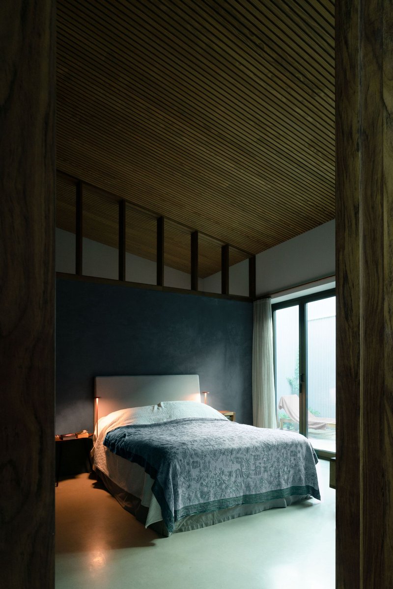 Bedroom framed by dark timber posts with slatted wood ceiling and blue plaster walls